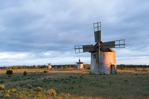 Windmills in Field in Gotland, Sweden at sunset with clouds behind them.