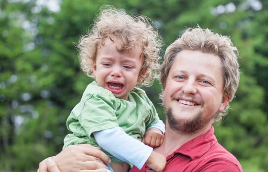 Portrait of 1 year old baby boy crying in father s arms.