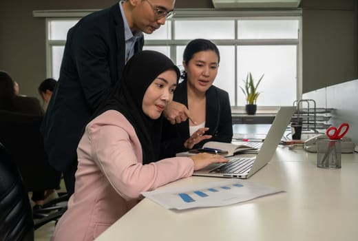 Group of three businesspeople working together in open plan office, they using laptop computer and paperwork.