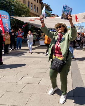 Istanbul, Turkey - May 13 2023: Woman dancing holding election campaign brochures in front of Republican Peoples Party kiosk in the neighbourhood of Ortakoy during the 2023 elections