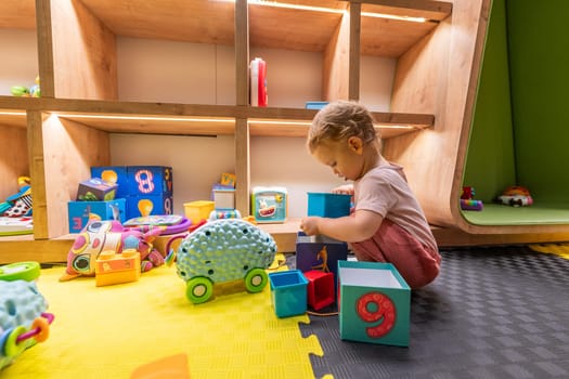 Toddler stacking colorful blocks and playing with toys in a bright learning playroom