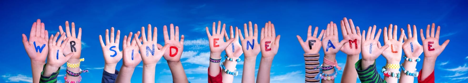 Children Hands Building Colorful German Word Wir Sind Eine Familie Means We Are Family. Blue Sky As Background.