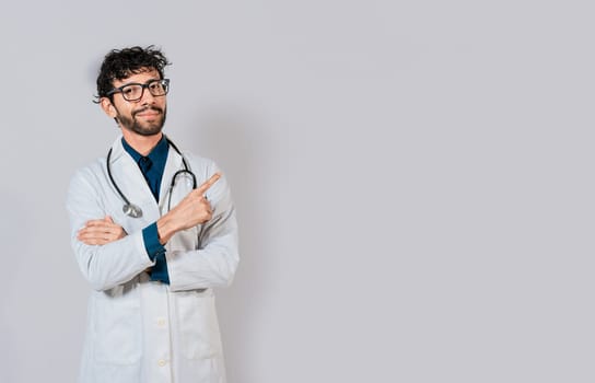 Smiling doctor pointing finger isolated. Doctor pointing at an isolated white space. Young doctor pointing finger at a blank space