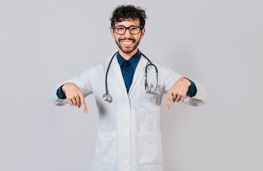 Young doctor pointing a promotion down. Handsome doctor pointing down an isolated advertising space. Happy doctor pointing fingers down