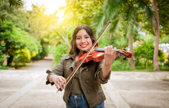 Young woman playing the violin outdoors. Portrait of a girl playing the violin outdoors, Close up of a girl with her violin playing a melody outdoors, Concept of smiling female violinist