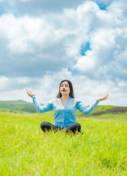 Young woman doing yoga on the grass in the field with blue sky in the background, Girl sitting doing meditation yoga in the field, woman doing yoga outdoors