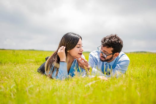 A couple lying on the grass looking at each other, young couple in love lying on the grass touching each other's faces, two people in love lying on the grass looking at each other