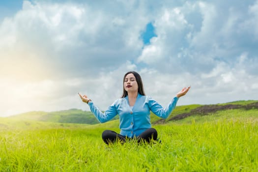 Girl sitting doing meditation yoga in the field, woman doing yoga outdoors, young woman doing yoga on the grass in the field with blue sky in the background.