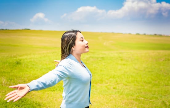 Happy woman breathing fresh air in the field and spreading arms, young woman smiling and spreading her hands in the green field, concept of woman breathing fresh air in the field