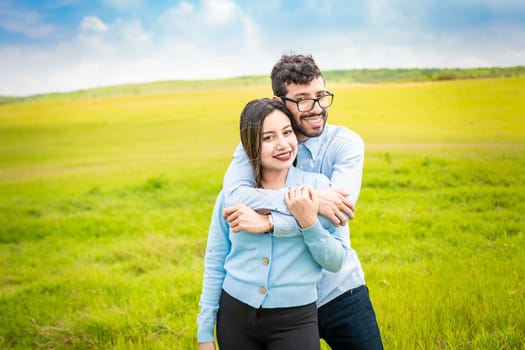 Portrait of a happy couple hugging in the field, Portrait of a young couple in love in the green field looking at the camera, Portrait of a cute couple in the field looking at the camera