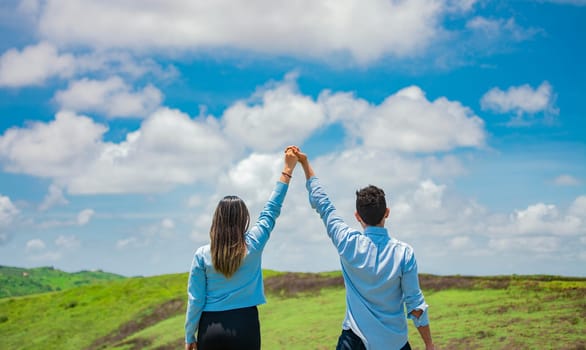 Back view of couple on the hill with hands raised to the sky, Happy couple in the field raising hands to the sky, Concept of a happy and free couple in the field