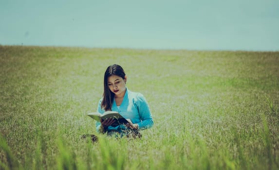 A girl reading a book in the field, A person sitting on the grass reading a book, Attractive people sitting on the grass reading a book
