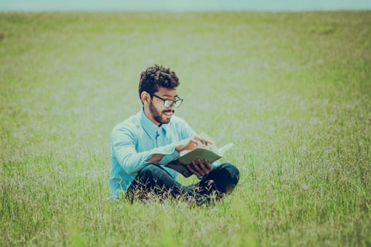 Young man on the grass reading a book, A person sitting on the grass reading a book, concept of people reading outside