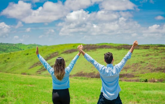 Back view of Happy couple in the field raising hands to the sky, Concept of a happy and free couple in the field, Back view of couple on the hill with hands raised to the sky