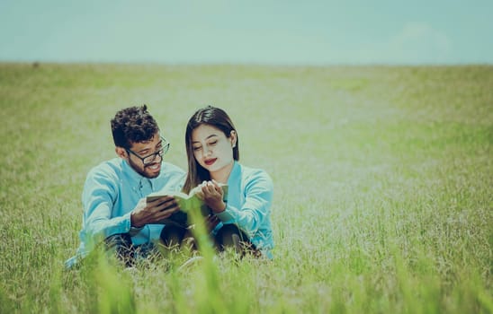 A couple sitting on the grass reading a book, Two people sitting on the grass reading a book, concept of people reading outside
