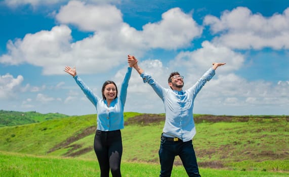 Concept of a happy and free couple in the field, Couple on the hill with hands raised to the sky, Happy couple in the field raising hands to the sky