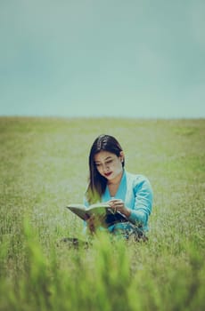 A person sitting on the grass reading a book, Attractive people sitting on the grass reading a book, A girl reading a book in the field