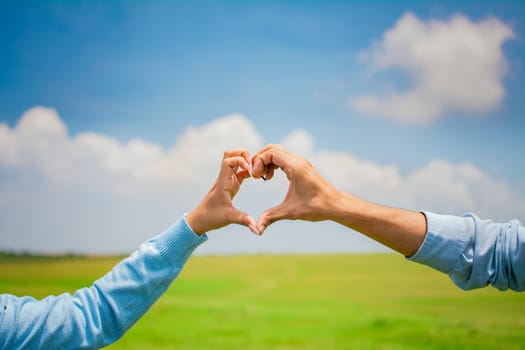 Close up of hands of a couple making a heart shape with hands, hands of a couple in love in the field making a heart shape, couple in the field making a heart shape with hands