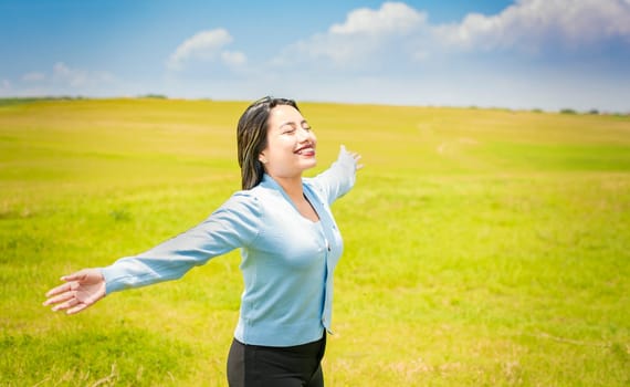 Young woman smiling and spreading her hands in the green field, concept of woman breathing fresh air in the field, Happy woman breathing fresh air in the field and spreading arms