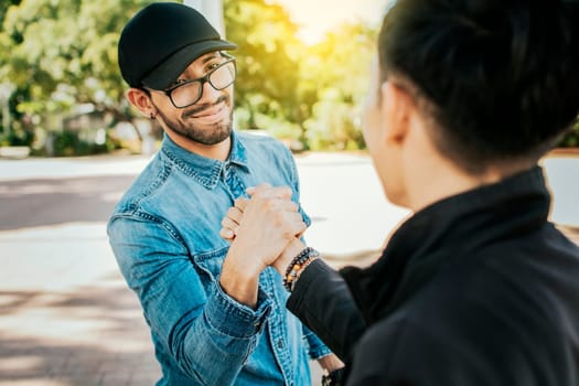 Concept of two friends greeting each other and shaking hands on the street. Two teenage friends shaking hands at each other outdoors. Two people shaking hands on the street