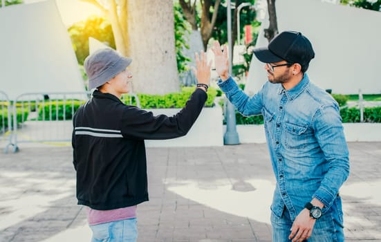 Side view of people greeting each other and shaking hands on the street. Two teenage friends shaking hands outdoors. Concept of two friends greeting each other with a handshake on the street