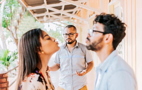 Man discovering his cheating girlfriend kissing another man in the street, Boyfriend discovering his girlfriend's infidelity outdoors. Man looking at his cheating girlfriend kissing another woman outdoors