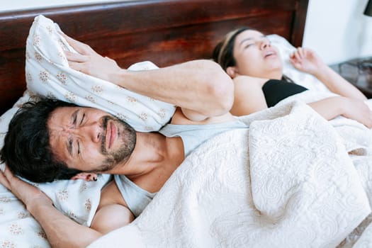 Woman snoring in bedroom and husband covering his ears. Husband suffering from the snoring of his sleeping wife. Sleep apnea concept