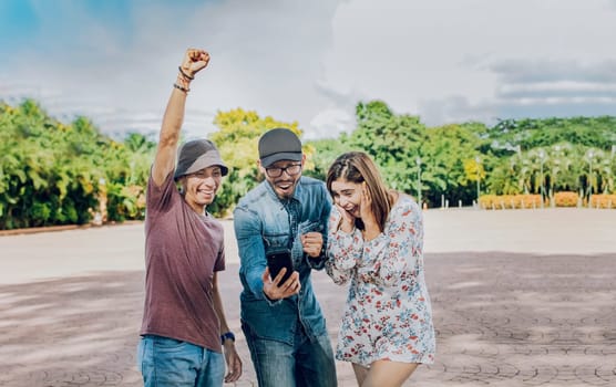 Three cheerful people looking at cell phone outdoors, Excited teenage friends looking at cell phone screen on the street. Three excited friends looking at the cell phone in the street