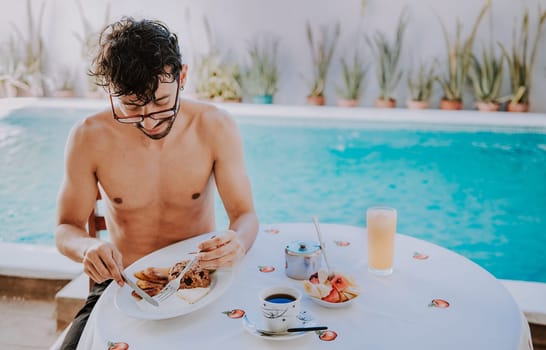 Young man on vacation in hotel having breakfast near swimming pool. Breakfast near the swimming pool. Person having breakfast in the hotel with pool in the background