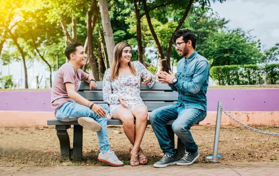 Three happy friends talking in a park. Three teenage friends talking sitting on a park bench, Group of three friends talking sitting in a park. Concept of people talking in the park