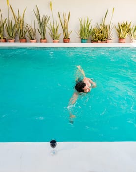 Man on vacation swimming in a blue swimming pool. Young man swimming in a tropical hotel pool. Handsome man on vacation swimming in a hotel pool
