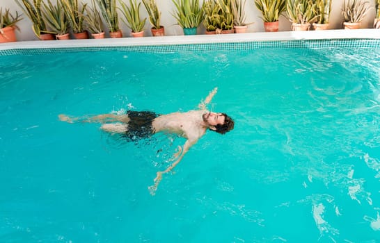 Young man swimming on his back in a hotel pool. Concept of man on vacation enjoying the pool, Man on vacation swimming on his back in a swimming pool