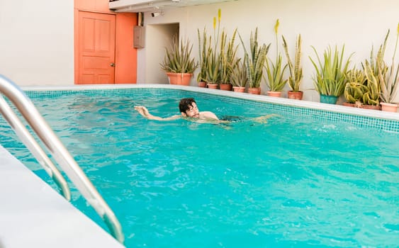 Young man swimming in a beautiful hotel pool, Man on vacation swimming in a blue swimming pool. Handsome man on vacation swimming in crystal clear pool