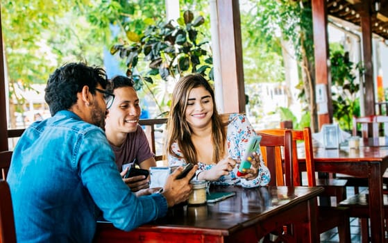 Young friends in a coffee shop with their cell phones having a good time. Three people in a coffee shop with phones having a good time. Three teenage friends on their cell phones in a coffee shop