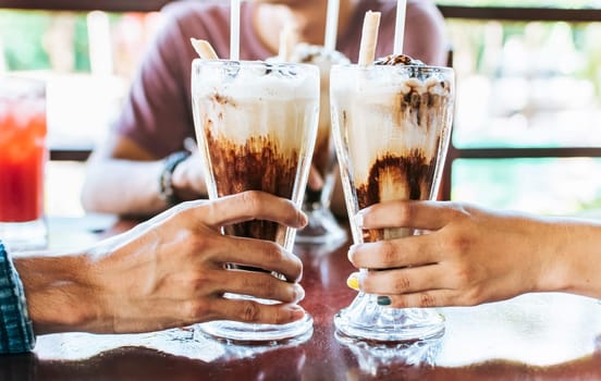 Man and woman hand toasting and holding two milkshake. Two hands toasting with milkshake in a cafe, Close up of two hands toasting with iced coffee in a cafe.