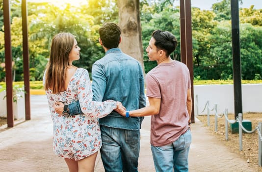 Unfaithful girl walking in the park with her boyfriend while holding another man hand. Love triangle concept. Woman holding hands with another man while walking with her boyfriend outdoor