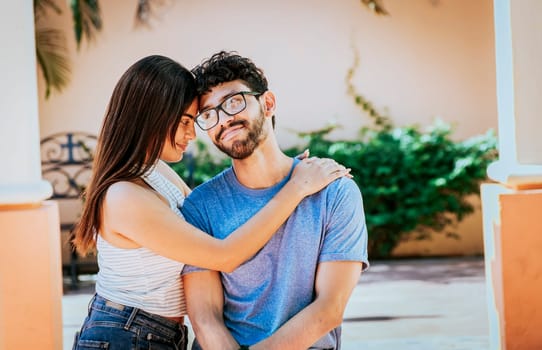 Attractive girl tenderly hugging her boyfriend outdoors. Girl hugging her boyfriend while he smiles at her, Happy couple, Girl hugging her boyfriend outside