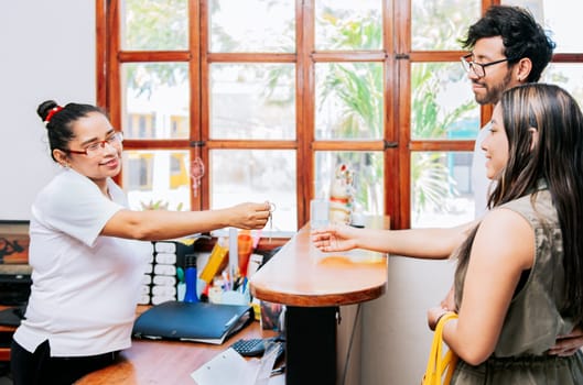 Latin couple receiving hotel room keys. Woman receptionist giving hotel room key to couple, Concept of couple arriving at hotel, Receptionist giving hotel room keys to couple