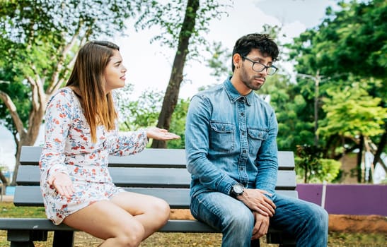 Upset couple arguing in a park. Girl arguing with her boyfriend sitting in a park, Young couple arguing and complaining sitting on a park bench, Concept of couple problems and jealousy