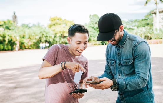 Two happy friends looking at a cell phone in the street, Two smiling friends looking at media on the cell phone in the street, Two young friends having fun with the cell phone outdoors