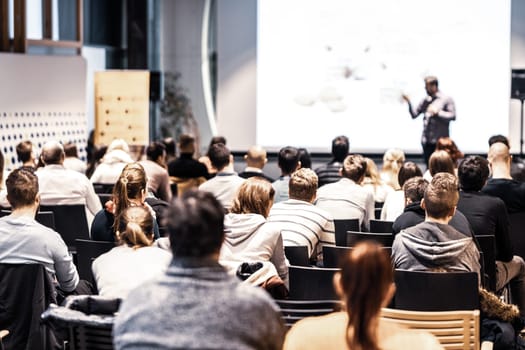 Speaker giving a talk in conference hall at business event. Audience at the conference hall. Business and Entrepreneurship concept. Focus on unrecognizable people in audience.