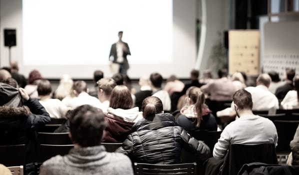 Speaker giving a talk in conference hall at business event. Rear view of unrecognizable people in audience at the conference hall. Business and entrepreneurship concept.