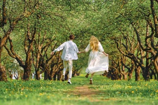 Back view of newlyweds hold hands of each other and run along trail in the park