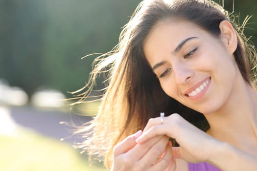 Happy fiancee looking at engagement ring sitting in a park