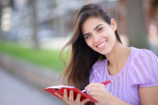 Happy woman writing in paper agenda looks at you in the street