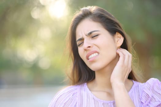 Stressed woman scratching neck after insect bite in a park