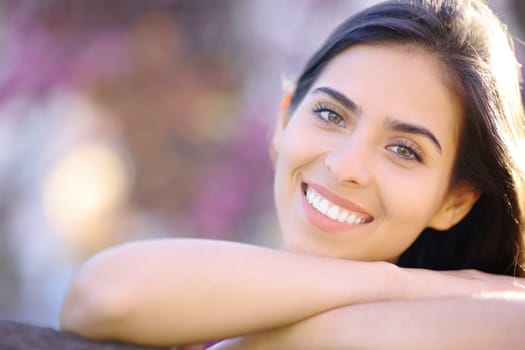 Front view of a beautiful woman with perfect white teeth smiling at you in a park