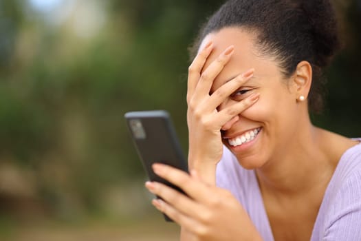 Embarrassed black woman using smart phone and looking at you
