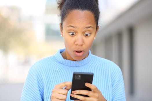 Front view portrait of a surprised black woman using cell phone in the street