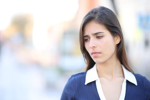 Sad woman complaining looking down walking in the street